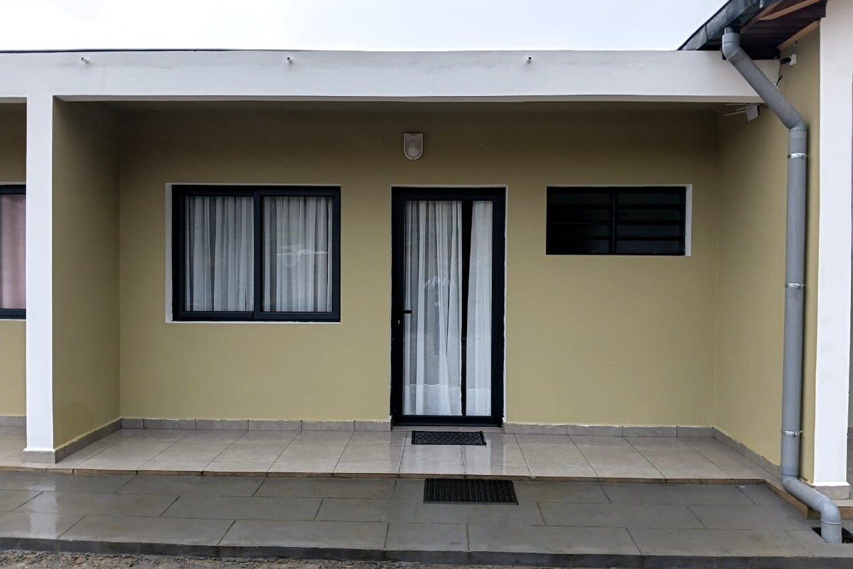 Un edificio con techo plano, puerta principal con panel de vidrio y una pequeña ventana con persiana.
