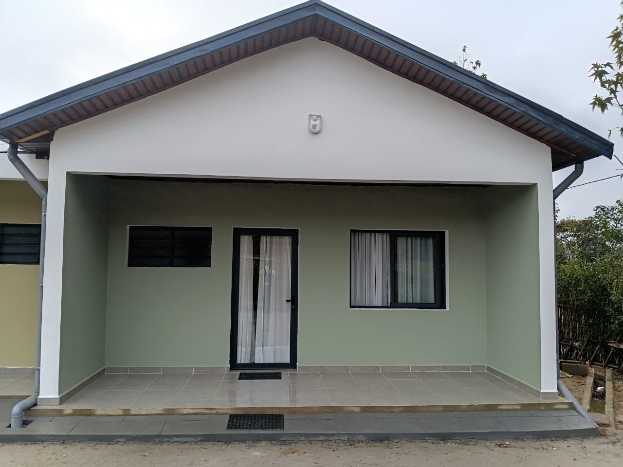 A single-story house with a flat roof, a front door, and two windows with curtains.