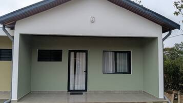 A single-story house with a flat roof, a front door, and two windows with curtains.