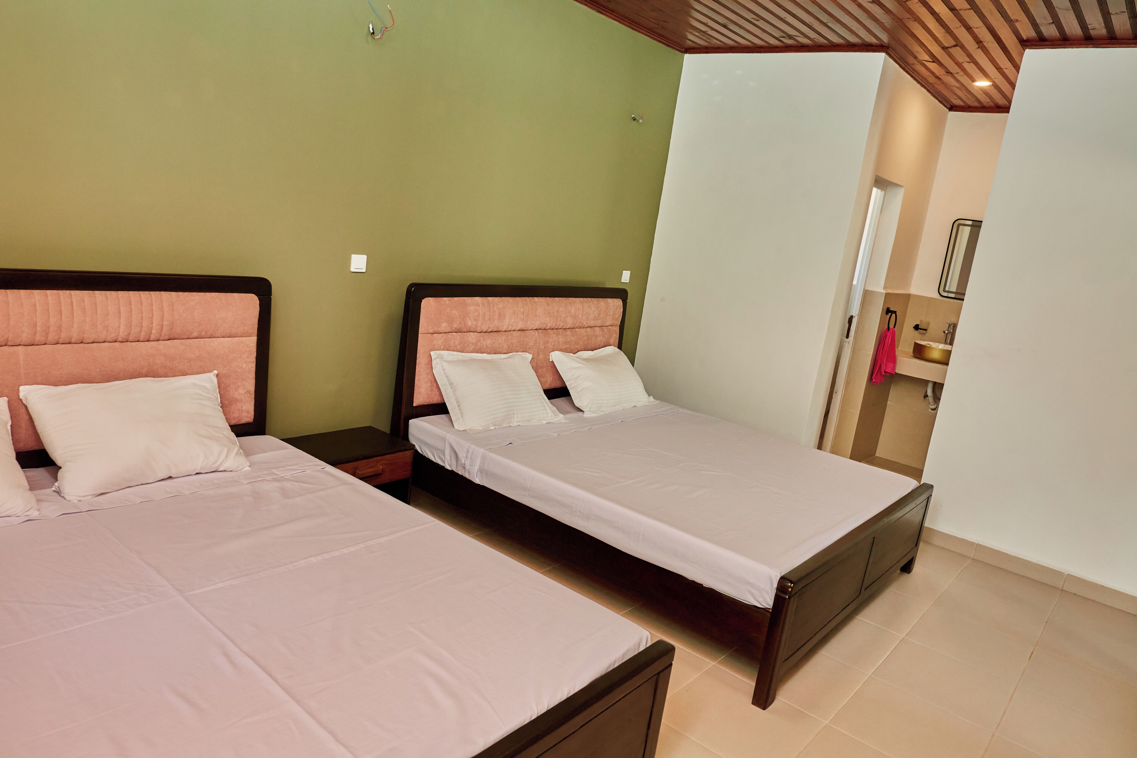 A hotel room with two beds, a wooden ceiling, and a bathroom visible through an open door.