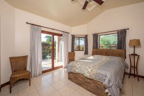 Une chambre à coucher avec un grand lit, deux fauteuils, une lampe sur pied et une vue sur l’extérieur grâce à une porte coulissante.