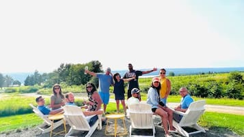 A group of people seated on white chairs outdoors with a view of a green landscape and a body of water in the distance.
