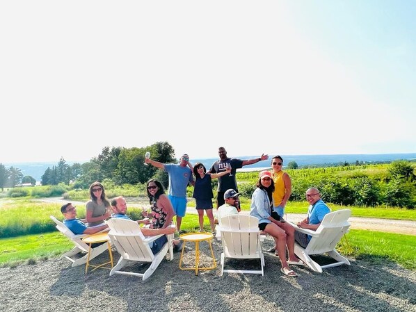 A group of people seated on white chairs outdoors with a view of a green landscape and a body of water in the distance.