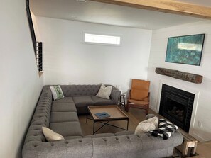 A modern living room with a sectional sofa, a coffee table, a fireplace, and a painting on the wall.
