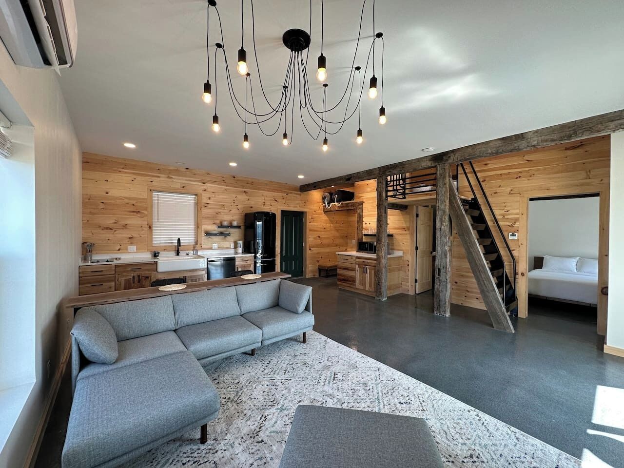 Un intérieur moderne avec un canapé d’angle, des murs en bois, un coin cuisine et un escalier.