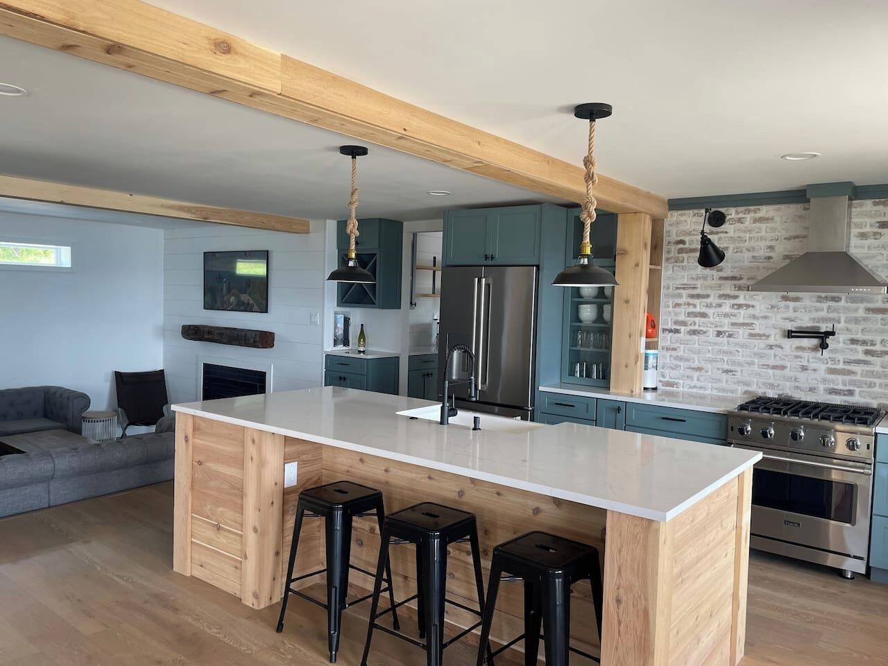A modern kitchen with a central island, bar stools, stainless steel appliances, and a stone backsplash.