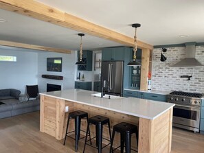Une cuisine moderne dotée d’un îlot central, de tabourets de bar, d’appareils électroménagers en acier inoxydable et d’un pare-feu en pierre.