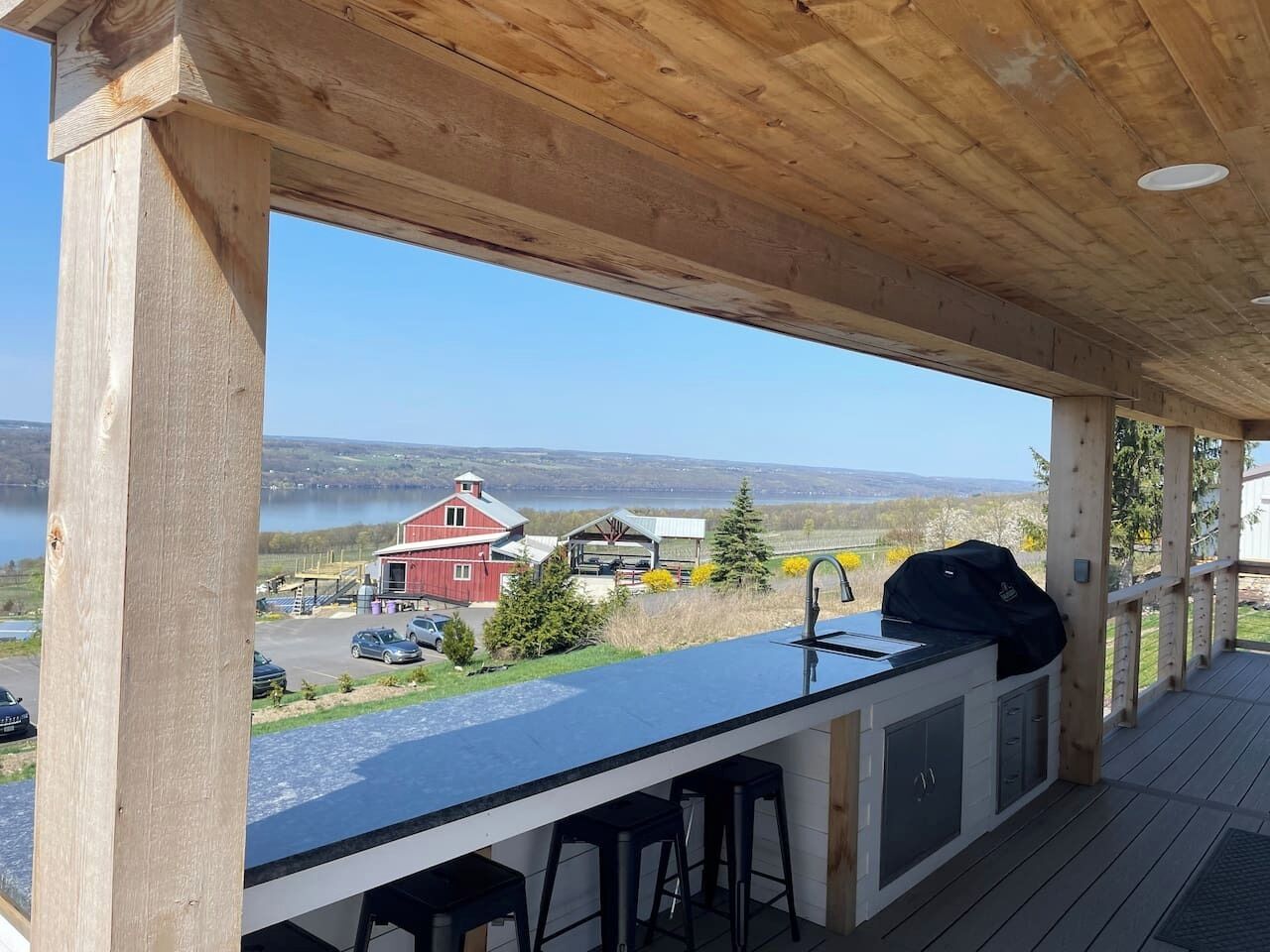 A covered outdoor area with a bar and seating, overlooking a lake and buildings.