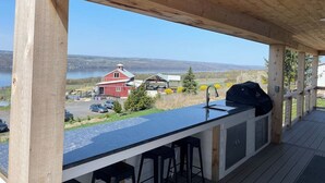 Ein überdachter Außenbereich mit Bar und Sitzgelegenheiten, mit Blick auf einen See und Gebäude.