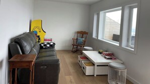 Ein gemütlicher Wohnbereich mit Sofa, Schaukelstuhl, kleinem Tisch und Fenster für natürliches Licht.