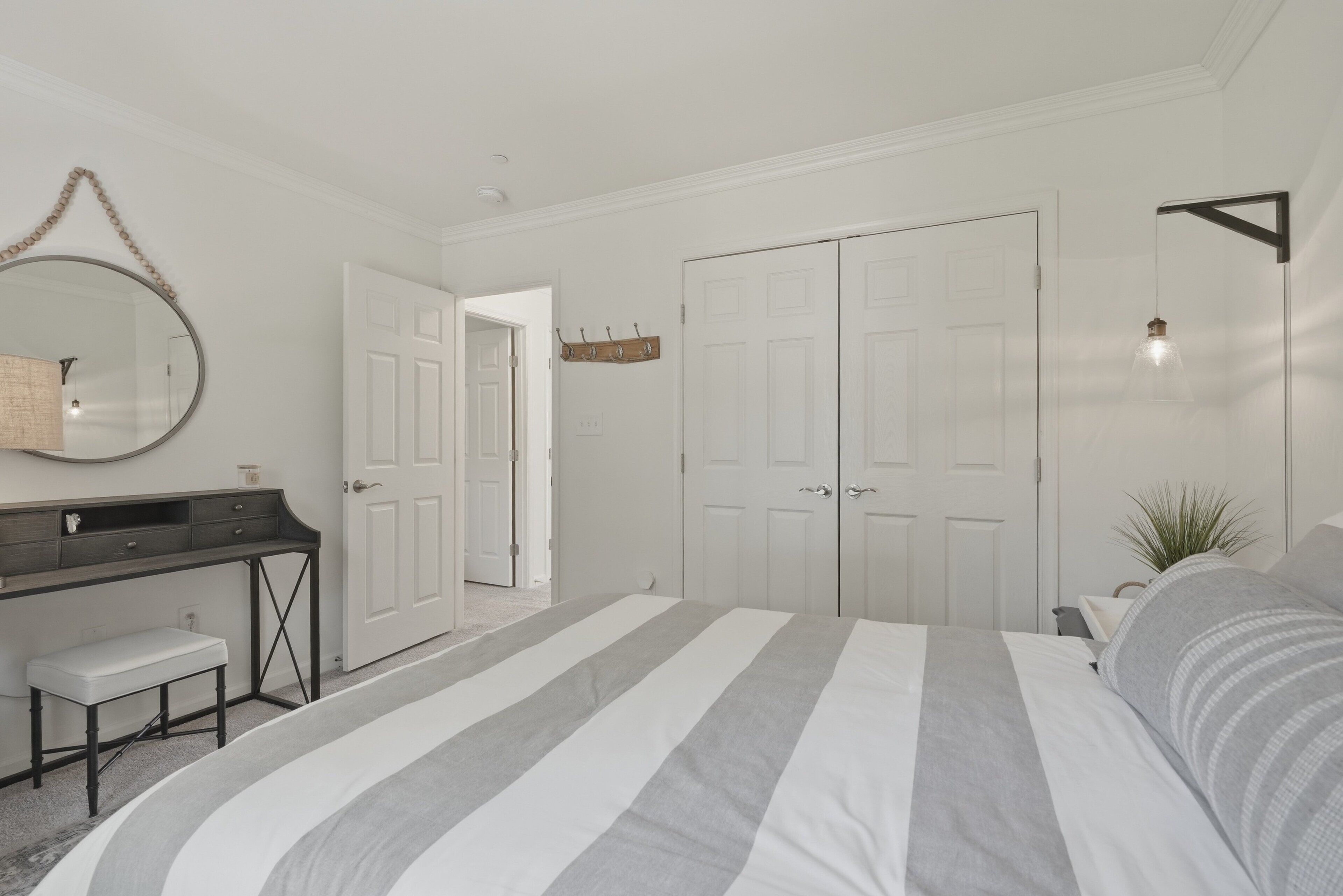 A bedroom with a bed, a desk, a chair, a mirror, a wardrobe, and a hanging light fixture.