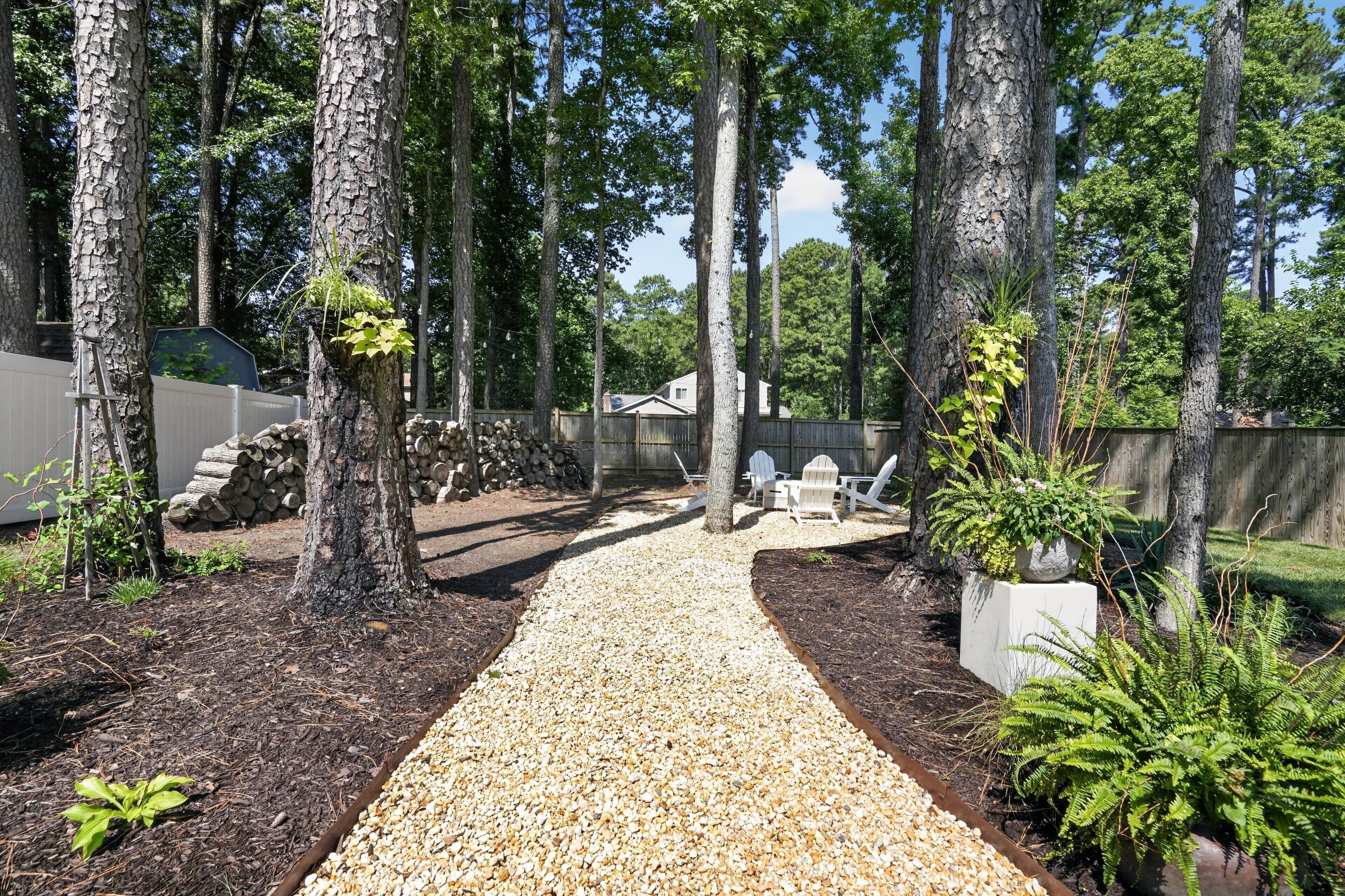 A gravel pathway leading through a wooded area with trees and a wooden fence.