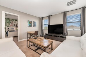 A living room with a TV, sofa, coffee table, and a view of the outdoors. - Epic Villa By Disney Theater Game Room Pool Spa (Davenport)