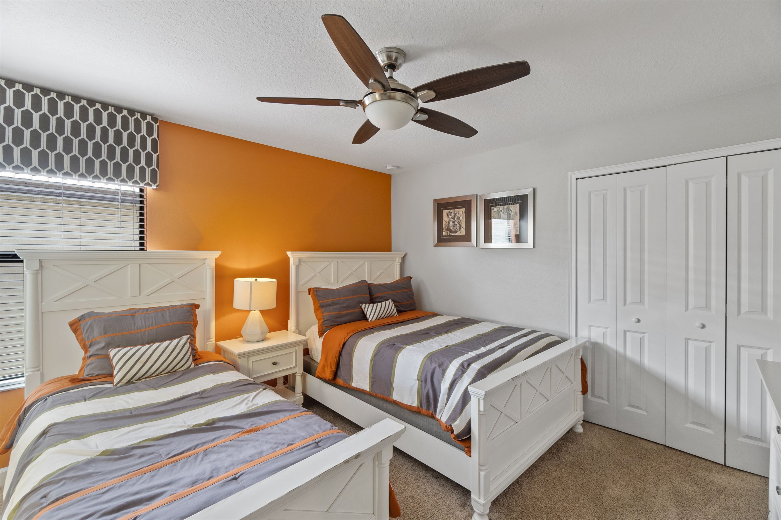 A bedroom with two beds, a ceiling fan, a window with blinds, and a door.