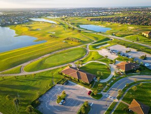 Ein Golfplatz mit zahlreichen Wasserhindernissen, einem Parkplatz und Wohnhäusern.