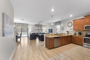 A modern kitchen with a central island, wooden cabinets, stainless steel appliances, and a dining area with a view to the outdoors. - Rolling Skies Poolside Cinema Free BBQ Near Disney (Davenport)