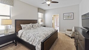 A bedroom with a bed, a ceiling fan, a dresser, a chair, and a painting on the wall. - Rolling Skies Poolside Cinema Free BBQ Near Disney (Davenport)