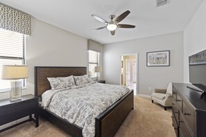 Ein Schlafzimmer mit Bett, Deckenventilator, Kommode, Stuhl und einem Bild an der Wand.
