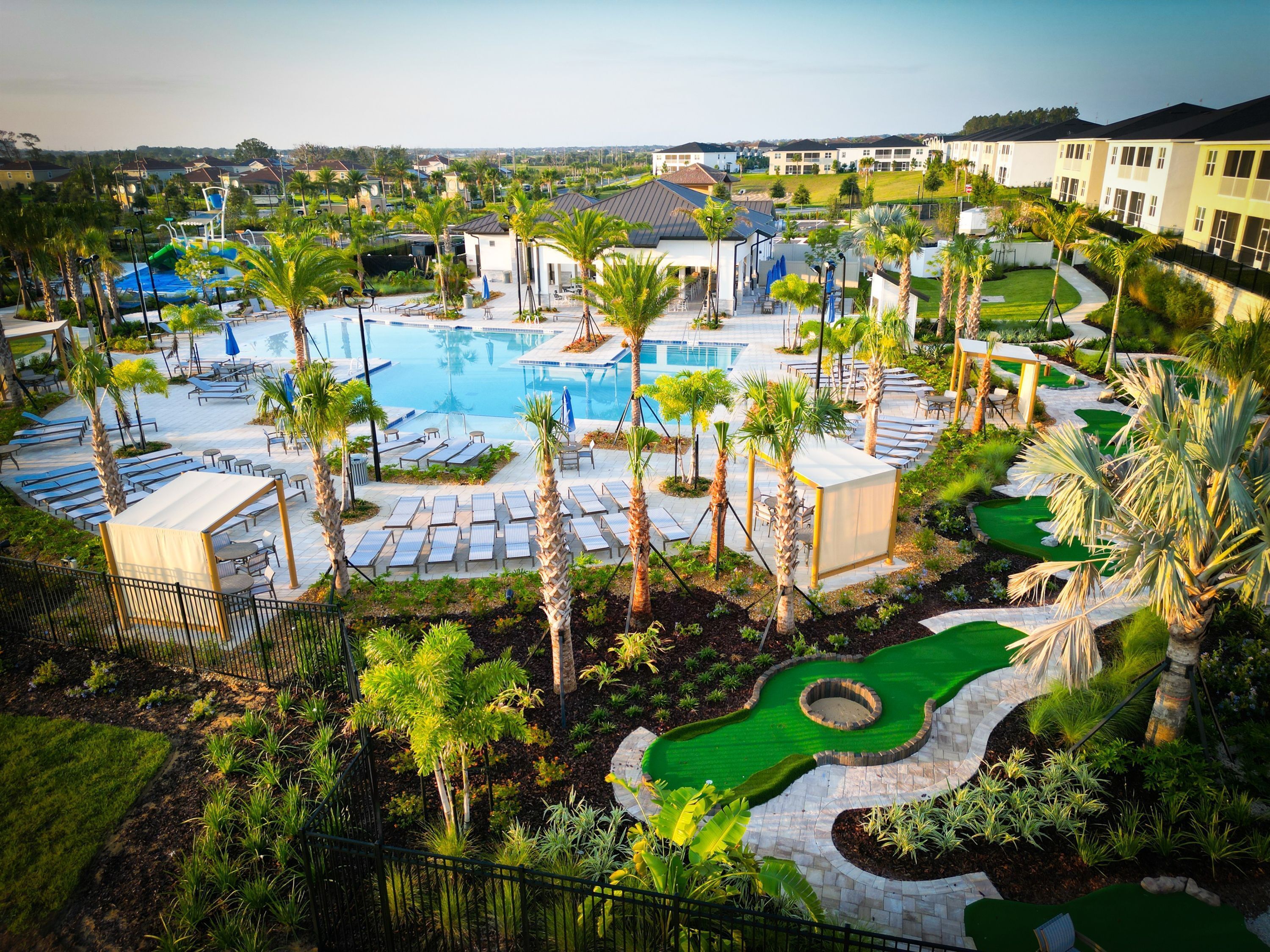 A resort with a swimming pool, sun loungers, palm trees, and a landscaped garden.
