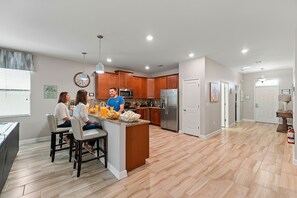 A modern kitchen with wooden cabinets, a stainless steel refrigerator, and a bar area with stools. - Rolling Skies Poolside Cinema Free BBQ Near Disney (Davenport)