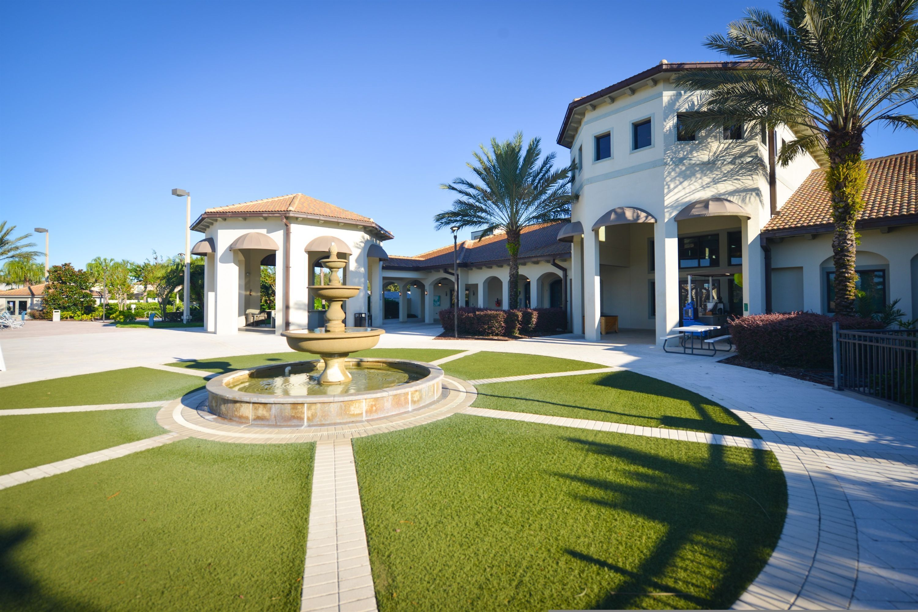 A courtyard with a central fountain, surrounded by a building with arched walkways and palm trees.