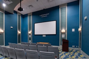 Une salle de conférence dotée d’un grand écran, de rangées de chaises, d’un pupitre et d’un mur bleu sur lequel est inscrit le texte « LENINAR HOMES ».