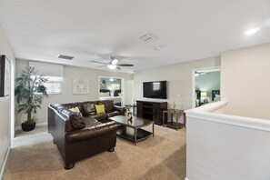 A living room with a brown leather sofa, a coffee table, a flat-screen TV, and a ceiling fan. - Rolling Skies Poolside Cinema Free BBQ Near Disney (Davenport)