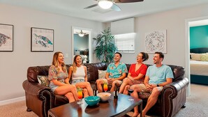 A living room with a brown leather couch, a coffee table with drinks, and artwork on the walls. - Rolling Skies Poolside Cinema Free BBQ Near Disney (Davenport)