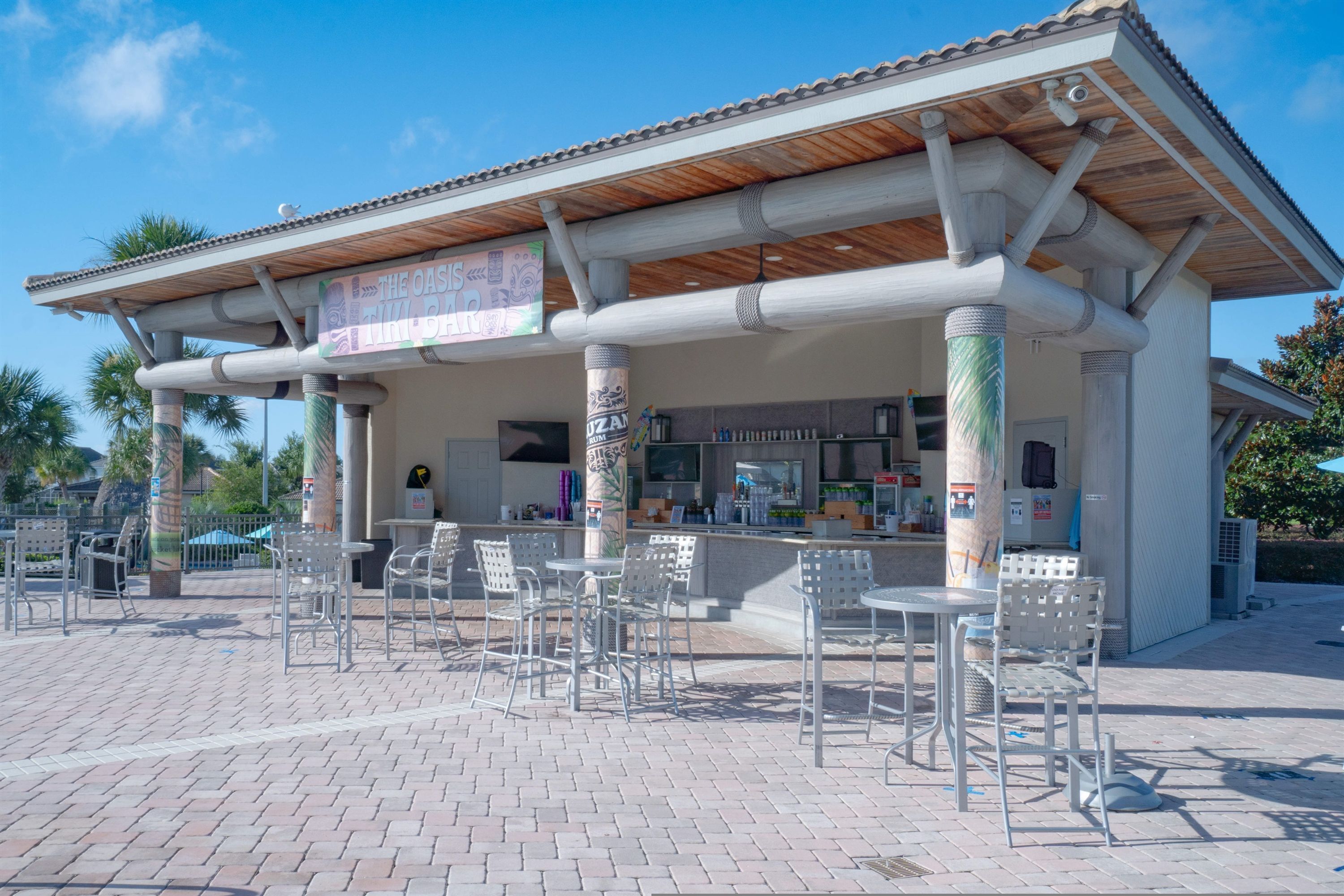 A covered outdoor seating area with metal chairs and tables, a bar counter, and a sign advertising 'The Oasis Bar'.