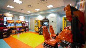 An arcade room with various gaming machines, a colorful carpet, and a door in the background. - Magical Retreat - Near Disney Heated Pool Spa (Davenport)