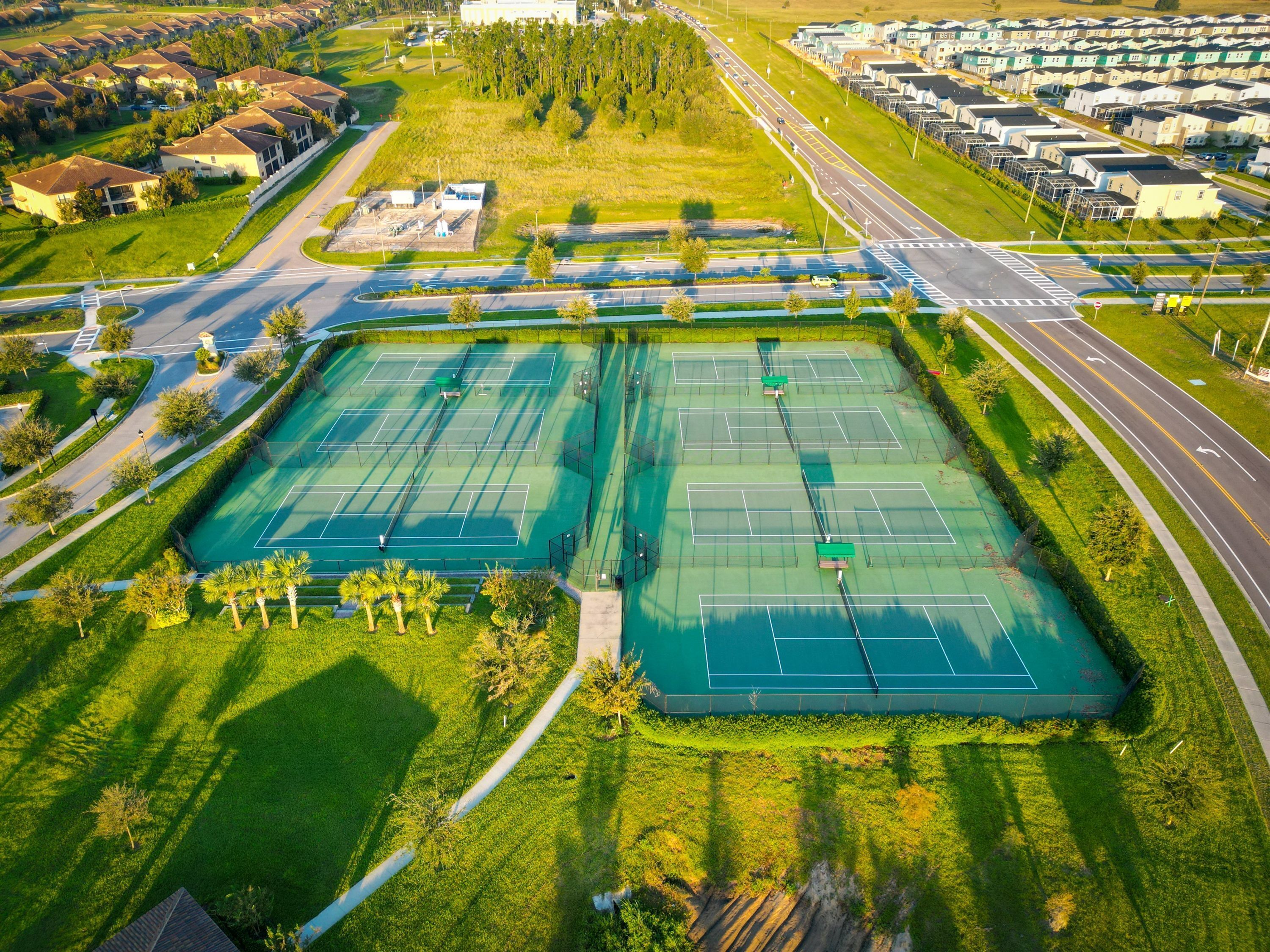 An aerial view of a residential area with multiple tennis courts, a road, and houses.