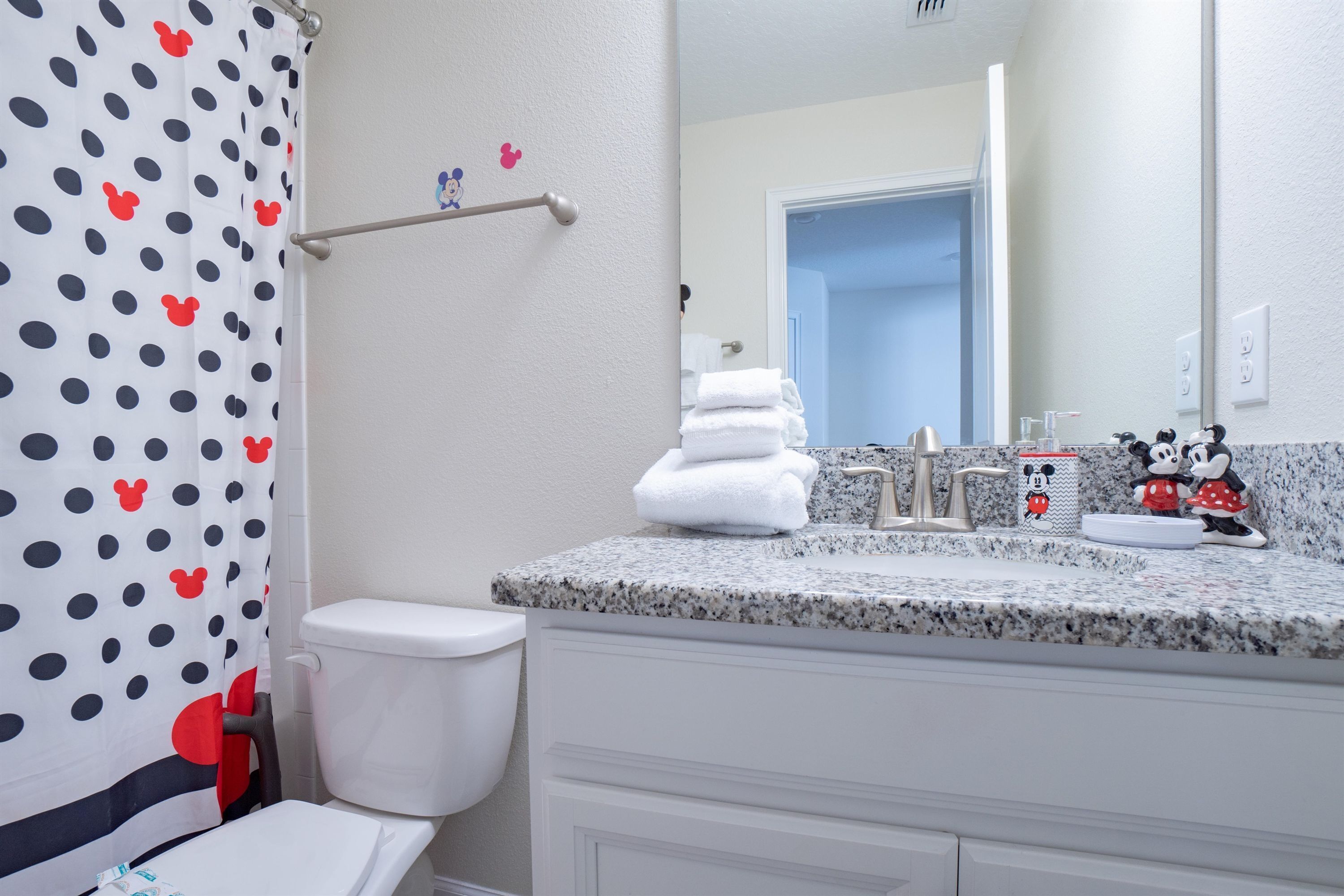 A bathroom with a white toilet, a sink with a granite countertop, and a shower curtain with a polka dot pattern.