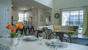 A dining area with a table set for a meal, a kitchen in the background, and a living area with a sofa and a view of the outside. - Magical Retreat - Near Disney Heated Pool Spa (Davenport)