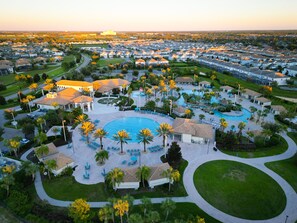 A residential area with a central swimming pool surrounded by palm trees and lounge chairs. - Magical Retreat - Near Disney Heated Pool Spa (Davenport)