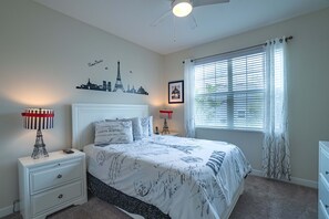A bedroom with a bed, a nightstand, a lamp, a window with blinds, and a wall decoration. - Magical Retreat - Near Disney Heated Pool Spa (Davenport)