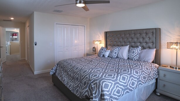 A bedroom with a tufted headboard, patterned bedding, a ceiling fan, bedside lamps, and a nightstand. - Magical Retreat - Near Disney Heated Pool Spa (Davenport)
