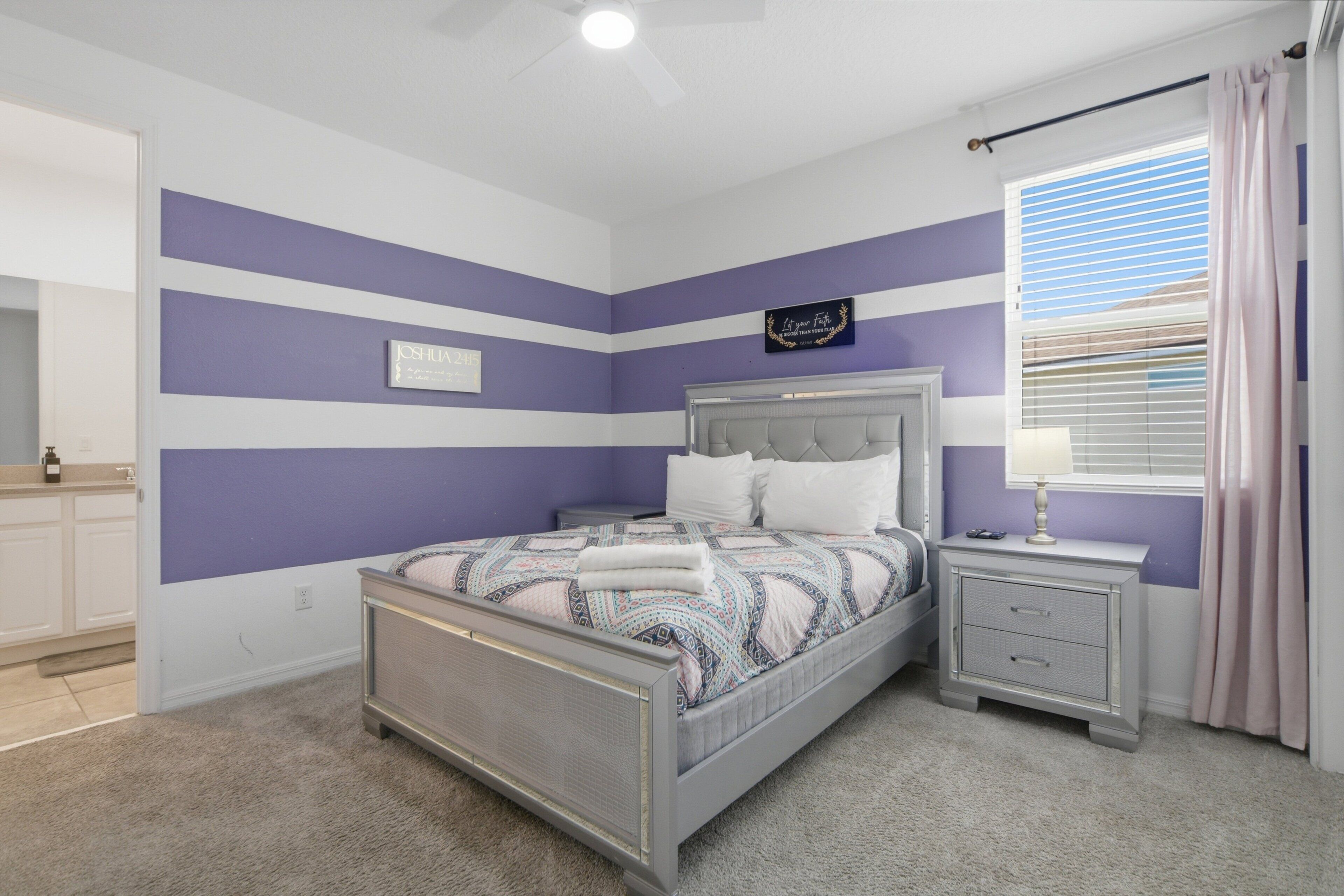 A bedroom with a bed, bedside tables, a nightstand, a window with curtains, and a wall with a sign.