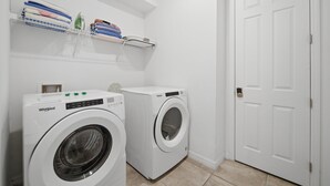 Una lavanderia con due lavatrici Whirlpool, una porta bianca e uno scaffale con asciugamani piegati e prodotti per la biancheria.
