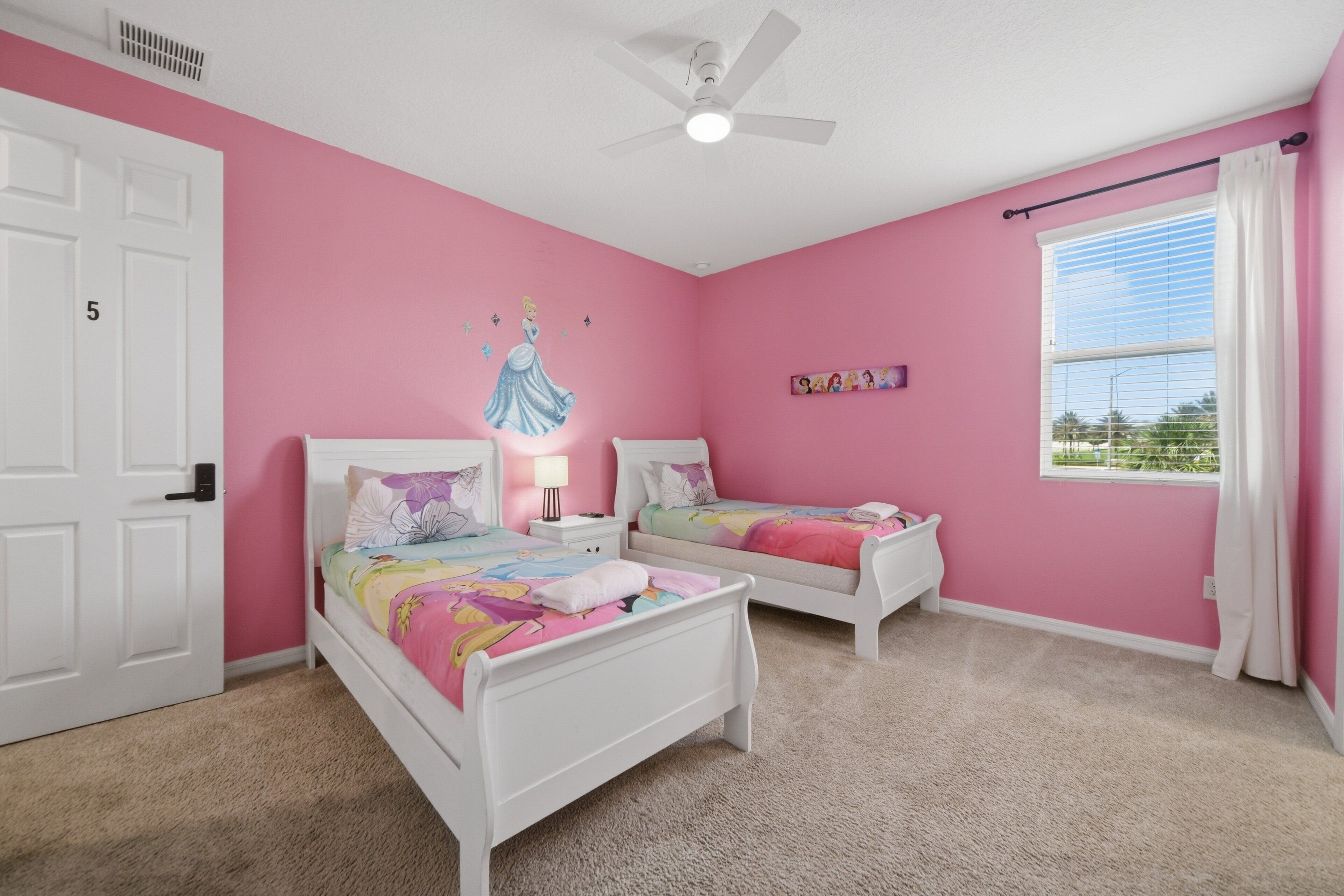 A bedroom with two white beds, a ceiling fan, a window with blinds, and a pink wall.