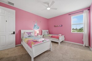 Une chambre avec deux lits blancs, un ventilateur de plafond, une fenêtre avec des stores et un mur rose.