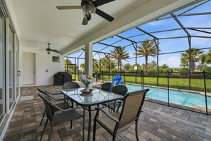 Ein überdachter Patio-Bereich mit Pool, Gartenmöbeln und Deckenventilator.