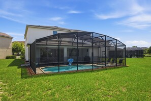 Une piscine couverte avec un panier de basketball, entourée d’une pelouse et d’une maison en arrière-plan.