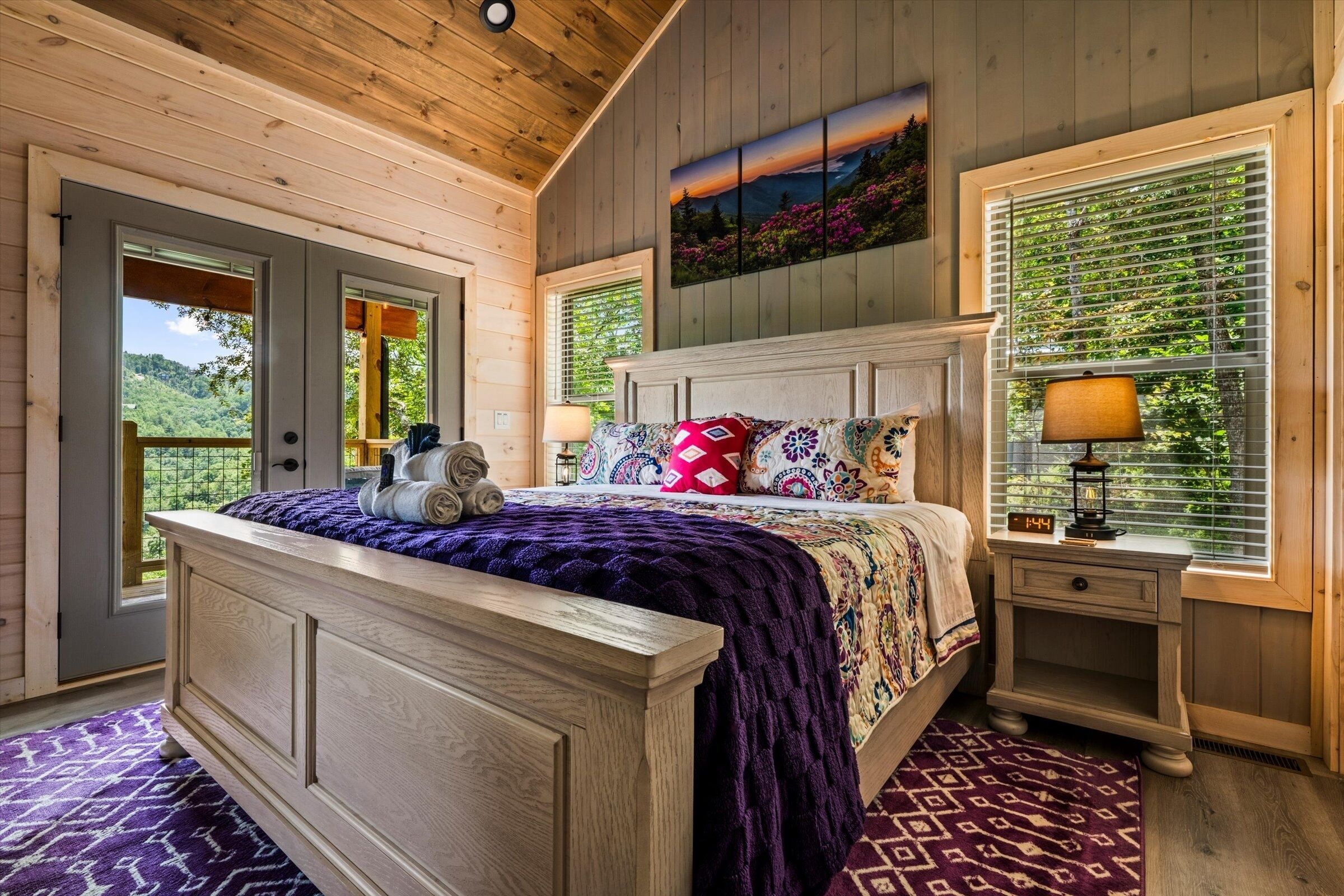 Une chambre à coucher avec un lit en bois, une table de chevet, une fenêtre avec des stores et une porte donnant sur l’extérieur.