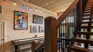 A wooden interior with a staircase, a Game Room Lounge sign, and colorful artwork on the wall. - Tennessee Sunrise 3 Bedroom Cabin (Sevierville)