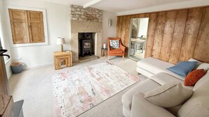 A living room with a stone fireplace, a sofa, a small table with a lamp, and a view through a wooden door.
