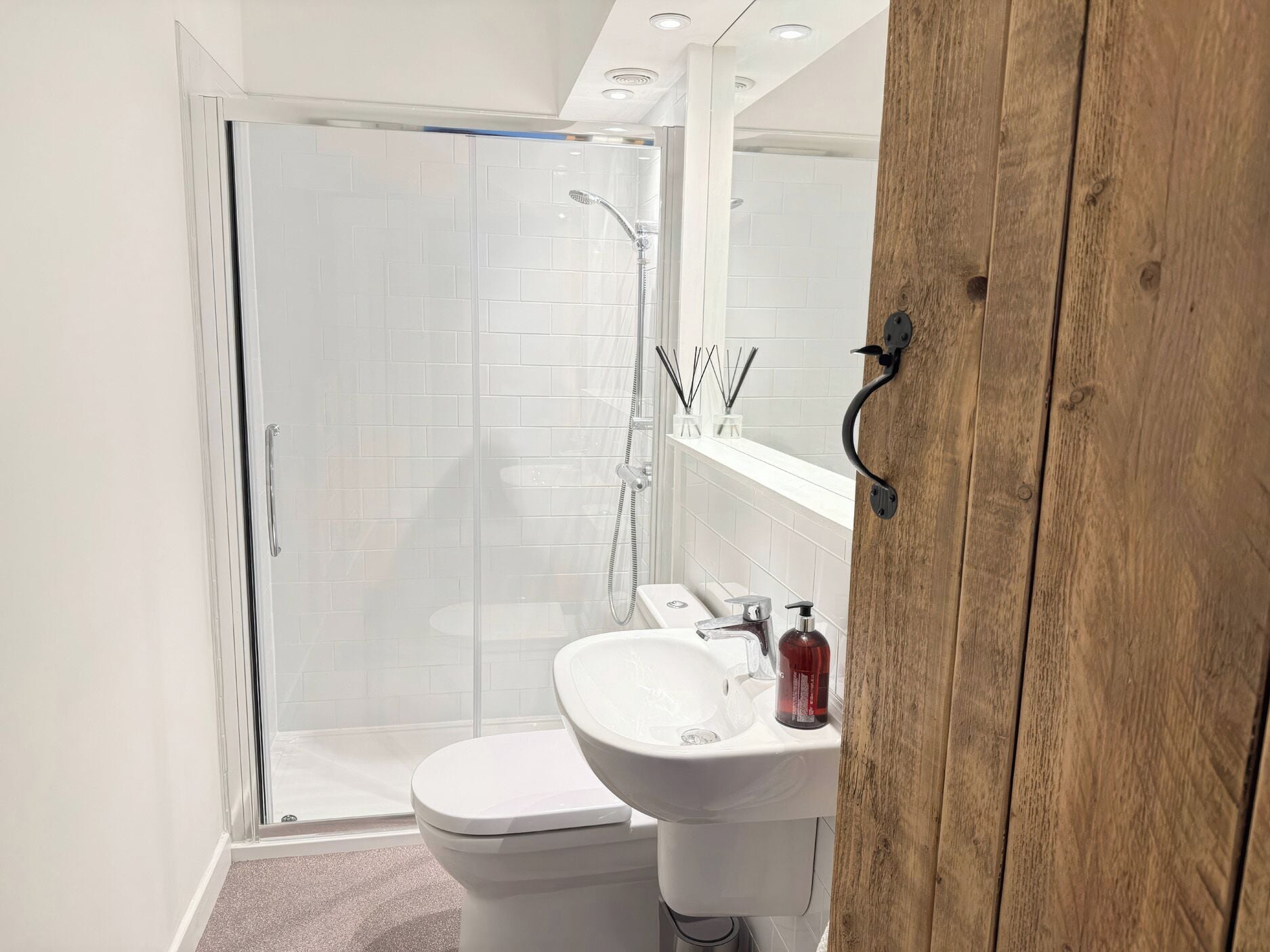 Un baño con cabina de ducha con puerta de vidrio, inodoro blanco y lavamanos con espejo.