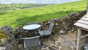 A stone patio with a round table and two chairs, overlooking a green field.