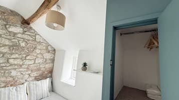 Een slaapkamer met een stenen muur, een bed met gestreept beddengoed, een hanglamp en een deur naar een inloopkast met hangende kleding.