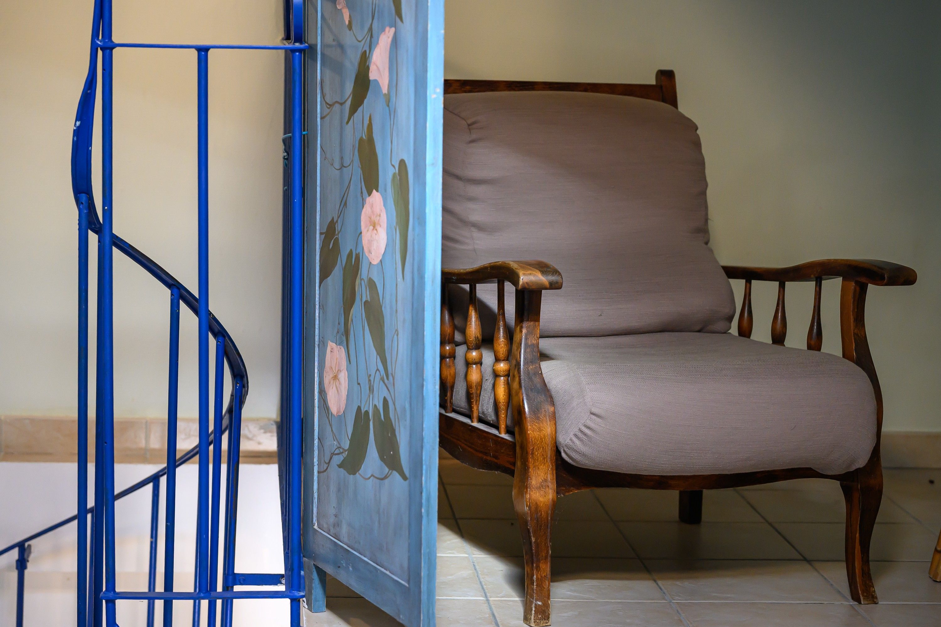 A chair with a cushioned seat and wooden frame, positioned next to a blue metal railing with floral patterns.