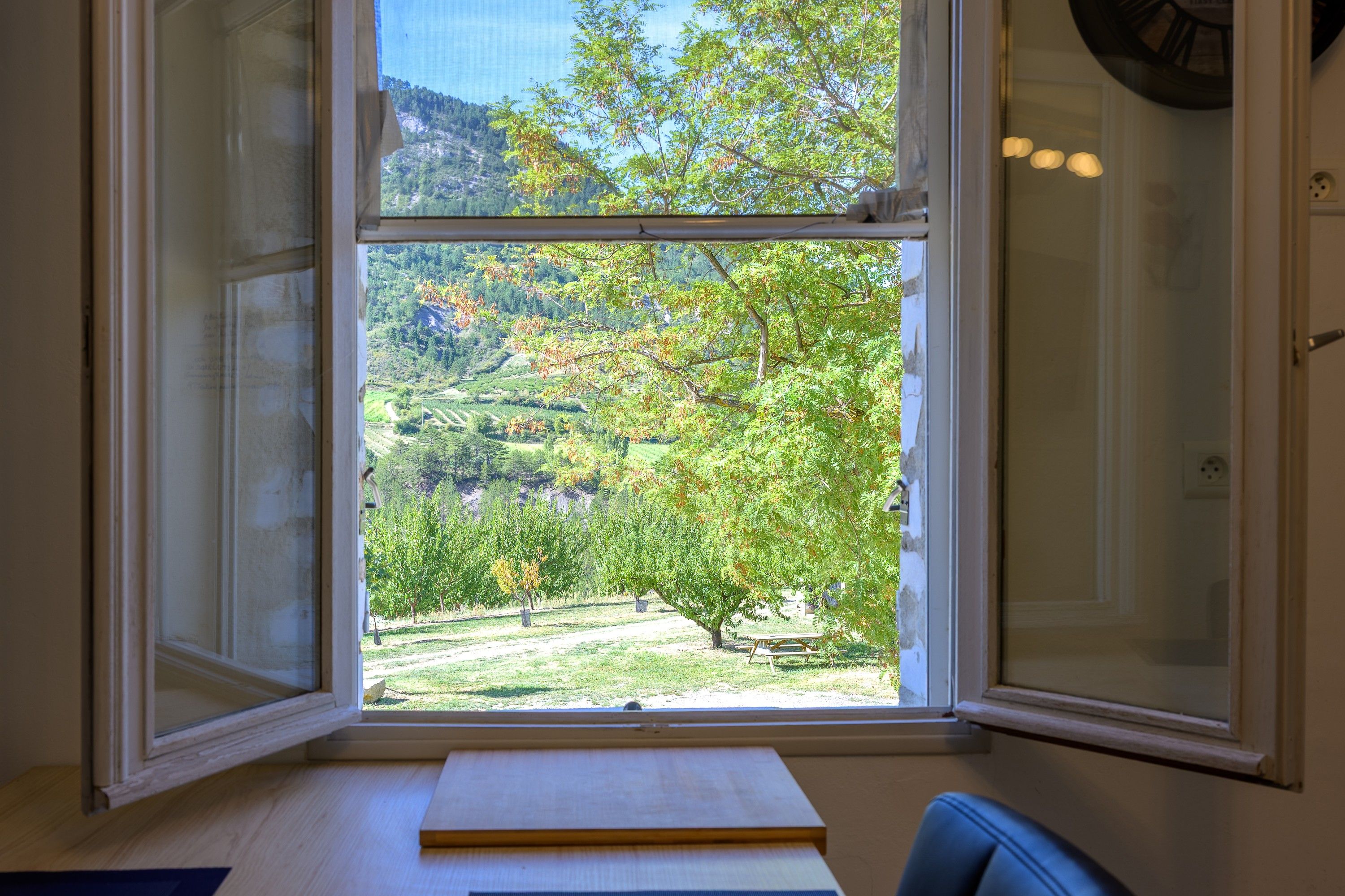 Een kamer met een groot raam, met uitzicht op een groen landschap met bomen en een heuvelachtige achtergrond.